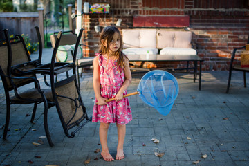 A small girl stands barefoot with a butterfly net in her hands.