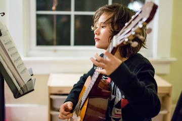 a boy studies sheet music as he practices guitar