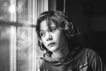 portrait of a young boy gazing out a window with a serious expression