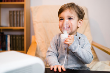 Little boy using steam inhaler nebulizer mask inhalation at home. Medical procedures vapor...
