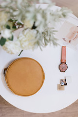 Bag, watch and barrette lie on a white table. Stylish concept. Flowers in a vase