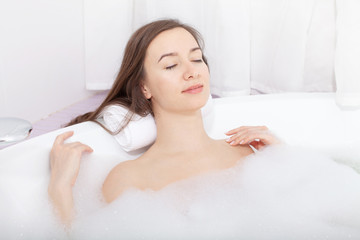 Obraz na płótnie Canvas Young pretty woman relaxes in bathtube with soap foam. Spa procedures in bathroom at home or hotelroom. Skin care and moisturizing for youth preservation.