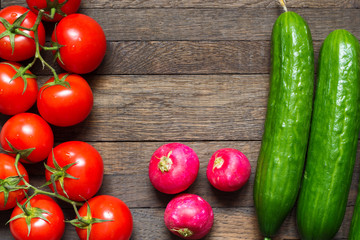 Ripe red tomatoes with radishes and cucumbers on wooden table.
