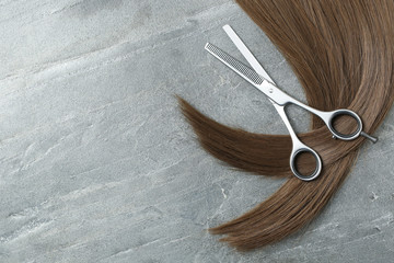 Flat lay composition with brown hair, thinning scissors and space for text on grey background. Hairdresser service