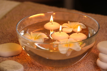 Bowl with water and burning candles on table in spa salon