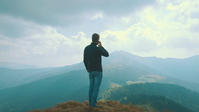 The male stands on a mountain and phones