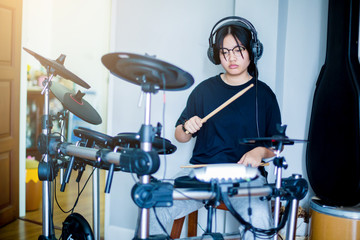 Asian girl put black tshirt and headphone learning and play electronic drum with wooden drumsticks...
