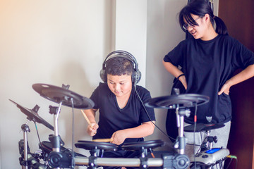 Asian girl and boy put black tshirt and headphone learning and play electronic drum with wooden drumsticks in home, smile and happy time in family.