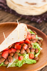 Fresh homemade vegan tacos made of folded flour tortilla stuffed with lettuce, cooked beans and tomatoes, served on wooden plate (Selective Focus, Focus  one third into the filling)