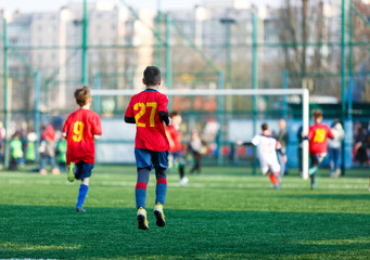 Boys at white red sportswear run, dribble, attack on football field. Young Soccer players with ball on green grass. Training, football, active lifestyle for kids  