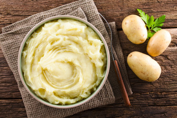 Fresh homemade creamy mashed potato in bowl, photographed overhead with fresh raw potatoes on the...