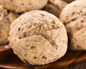 Fresh homemade wholegrain bread rolls with linseeds and sunflower seeds on wooden plate (Selective Focus, Focus on the front of the first bread roll)