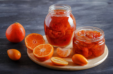 Fototapeta na wymiar Tangerine and kumquat jam in a glass jar on a black wooden background.