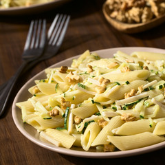 Penne pasta with zucchini and ham stripes and walnut, photographed on dark wood with natural light (Selective Focus, Focus in the middle of the dish)