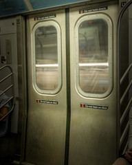 New York City Subway doors, closed, while train is moving, with light-streaks visible through the...