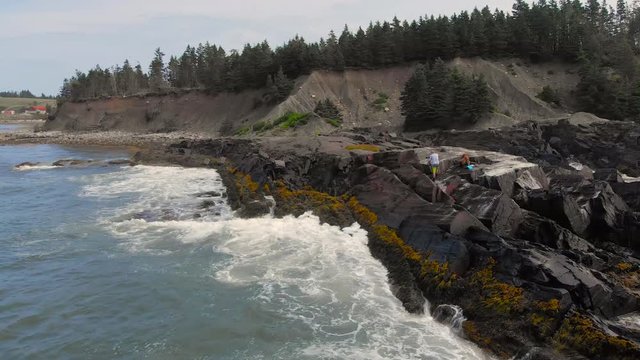 Cinematic drone / aerial static footage showing a bay, someone taking pictures on the rocks and a dog in the cost of Kingsburg, Nova Scotia, Canada during summer season.