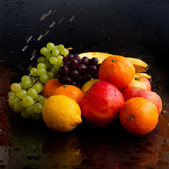 Beautiful juicy fruits on a black wet background: apples, grapes, oranges, bananas, copy space, close-up, square