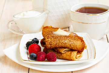 Healthy breakfast, homemade classic russian pancakes with fresh berry and sour cream, white wooden background. Sweet Homemade Stack of Pancakes with Butter, fresh forest berries and cream with tea.