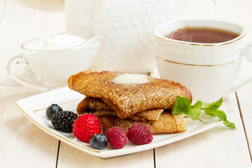Pancakes with berries, yogurt and tea in a white porcelain Cup. Healthy summer breakfast, homemade...