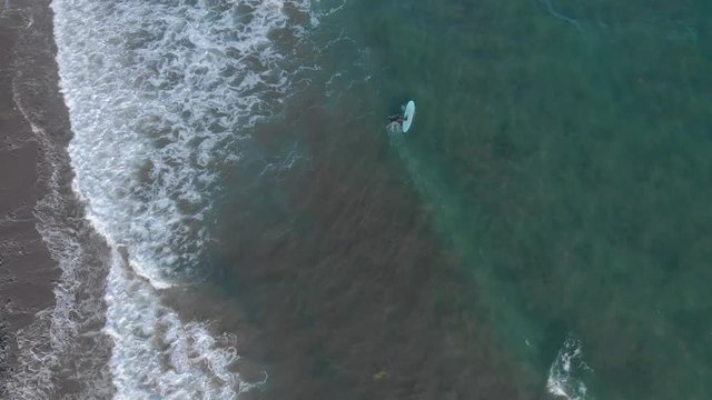 Cinematic drone / aerial footage rolling up the camera showing a couple of surfers and waves hitting the beach at Cole Harbour coast in Lawrencetown, Nova Scotia, Canada during summer season.