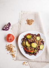 Vegetarian salad of purple cabbage, germinated wheat, tomatoes and avocado on linen tablecloth, top view.