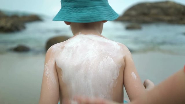 Mother applying sunblock cream on son back at beach.