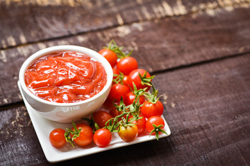 Ketchup in cup and fresh tomatoes on white plate / Close up tomato sauce on wooden dark background