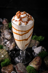 Milkshake. Cold drink of milk, ice cream, chocolate and caramel on a black background with stones and ice. Cocktail card for a bar or restaurant.