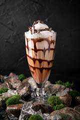 Milkshake. Cold drink of milk, ice cream, chocolate and caramel on a black background with stones and ice. Cocktail card for a bar or restaurant.