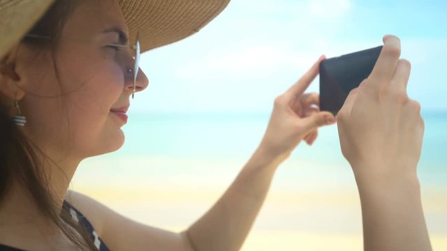 young traveler woman in hat taking photo on smartphone in ocean beach