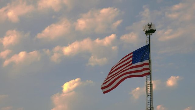 US flag attached to a fire truck ladder waves on a partly cloudy windy day