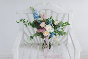 Beautiful and stylish wedding bouquet with roses lies on a white wooden chair in a modern studio. Wedding details and decorations.