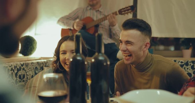 Young boys and girls having fun in a friendly atmosphere. They sing songs with guitars and laugh. Happy company celebrates a holiday in a cozy atmosphere.