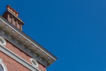 Exterior brick building with large chimney, round windows, and carved corbels, blue sky copy space,...