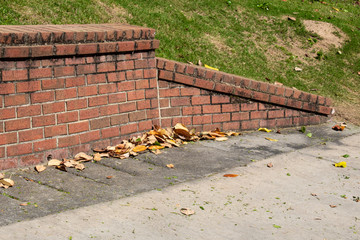 Sloped end piece of old brick retaining wall, concrete with magnolia leaves, horizontal aspect