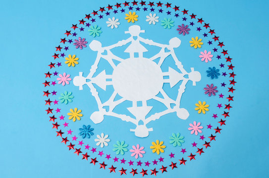 Paper doll chain and circles made from flowers and stars confetti against blue background