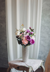 A wedding bouquet of multi-colored roses is in a vase, on a stand in a modern studio. Beautiful scenery and details.