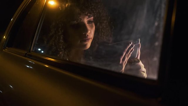 Beautiful Afro American woman tourist traveling in a taxi and rewritten with your friends on your phone at night.  Passenger Girl looking at cellphone at night in the back seat of a car.