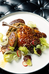 Close up photo of a juicy duck leg confit served with foie gras, sliced radish, and green salad 
