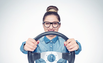 Happy young girl with glasses and car steering wheel, front view, auto concept 