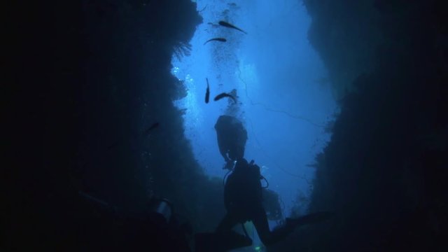 camera films from inside an submerged cave where divers are diving into. you see silhouettes of scuba divers