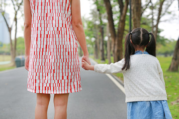 Close-up mom and daughter holding hands in the outdoor nature garden. Back view.