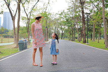 Happy Asian mom and daughter walking on street in the summer park.