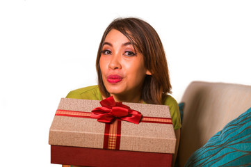 young beautiful and happy Asian Indonesian woman holding birthday or Christmas present showing the gift box cheerful and excited sitting on living room couch
