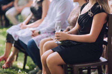Invited to the wedding girl in a black dress sitting on a chair with a glass of champagne. Wedding...