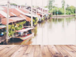Wooden table top over abstract blur background of vintage riverfront house in Thailand.