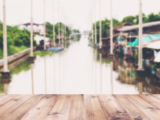 Wooden table top over abstract blur background of vintage riverfront house in Thailand.