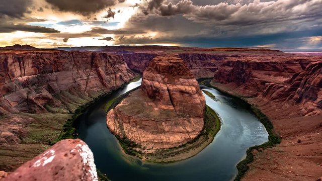 Motion controlled time lapse of a breathtaking natural meander bend in a large river flowing through a canyon at sunset with dark and fierce storm clouds.