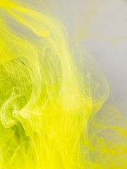 Transformation of ink droplet in water, close up view. Blurred background. Yellow paint dissolving into water, abstract pattern. Acrylic clouds in liquid, abstract background. Ink swirling in liquid