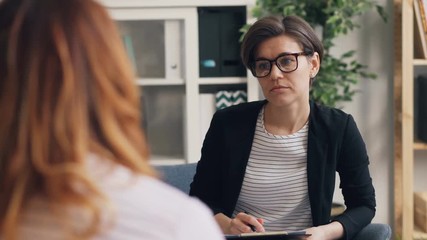 Successful doctor psychologist is consulting female patient in office talking and writing listening to symptoms. Psychology, profession and communication concept. - Powered by Adobe